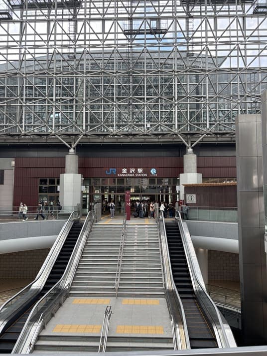 金沢駅の改札前。ガラスと鉄骨で組まれたもてなしドームの天井の下、エスカレーターと階段が伸びている