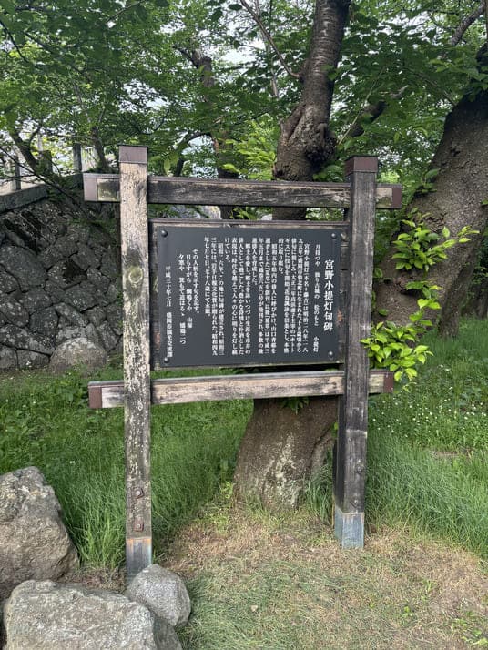 石垣と大木を背にした「宮野小提灯句碑」の案内板
