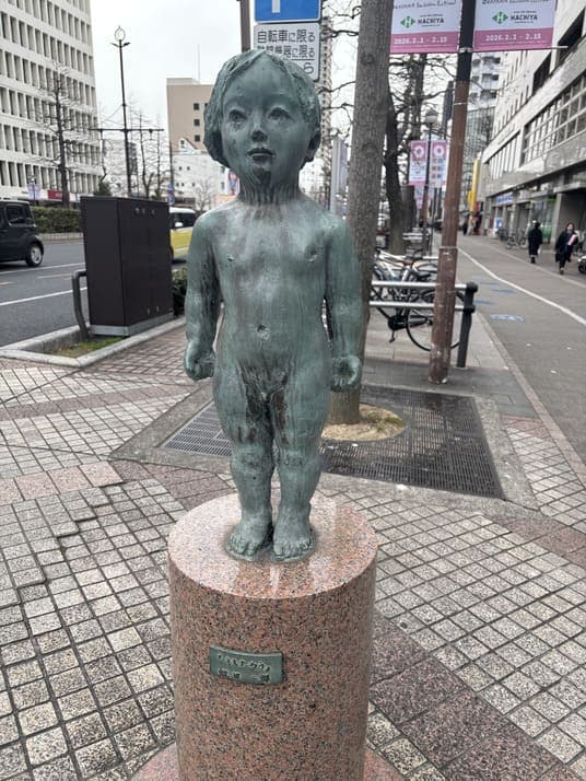 街角の歩道に立つ、子どもをかたどった銅像
