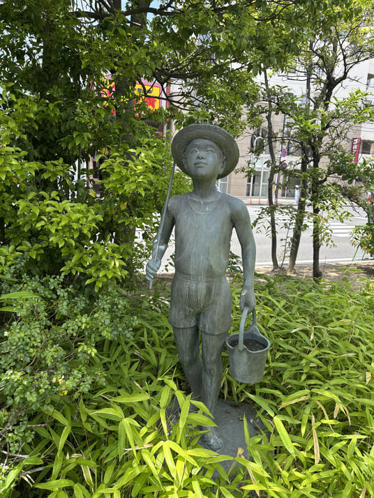 麦わら帽子をかぶり、手桶を提げた少年の銅像