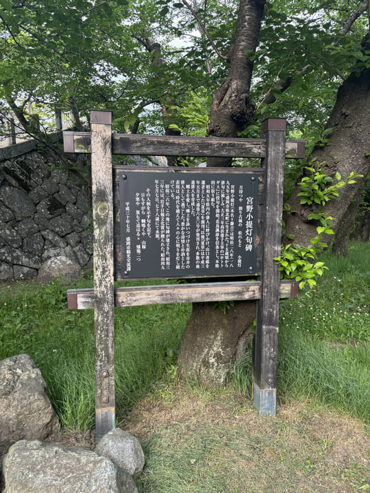 石垣と大木を背にした「宮野小提灯句碑」の案内板