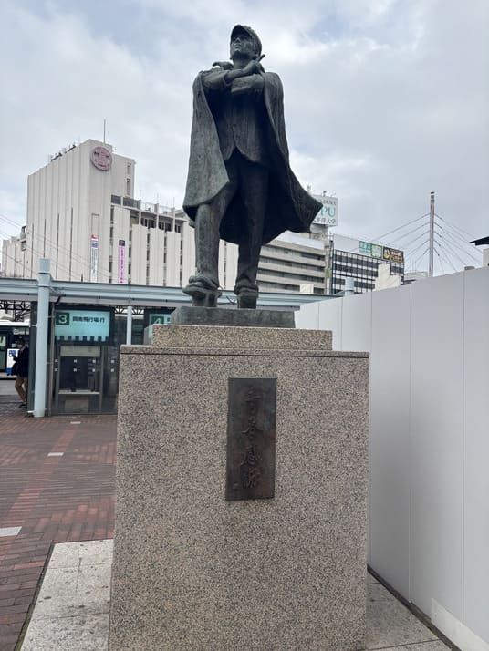 岡山駅前広場に立つ、マントをまとった人物の銅像