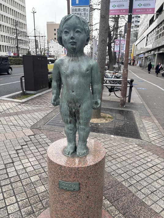 街角の歩道に立つ、子どもをかたどった銅像