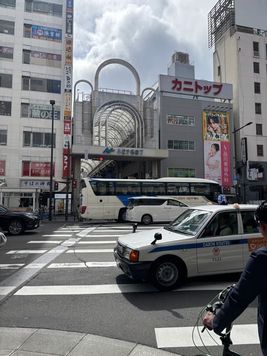 アーチ状の屋根が架かるアーケード商店街の入口と、駅前の交差点